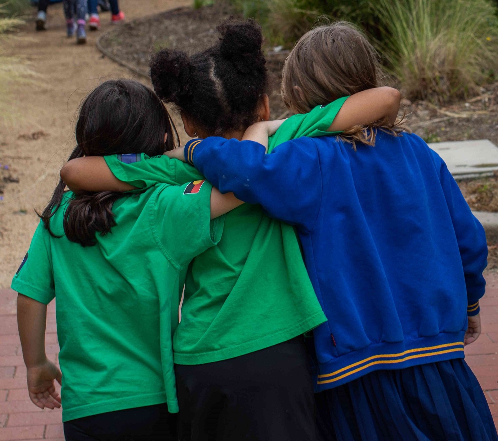 Three children walking with their arms around each other 